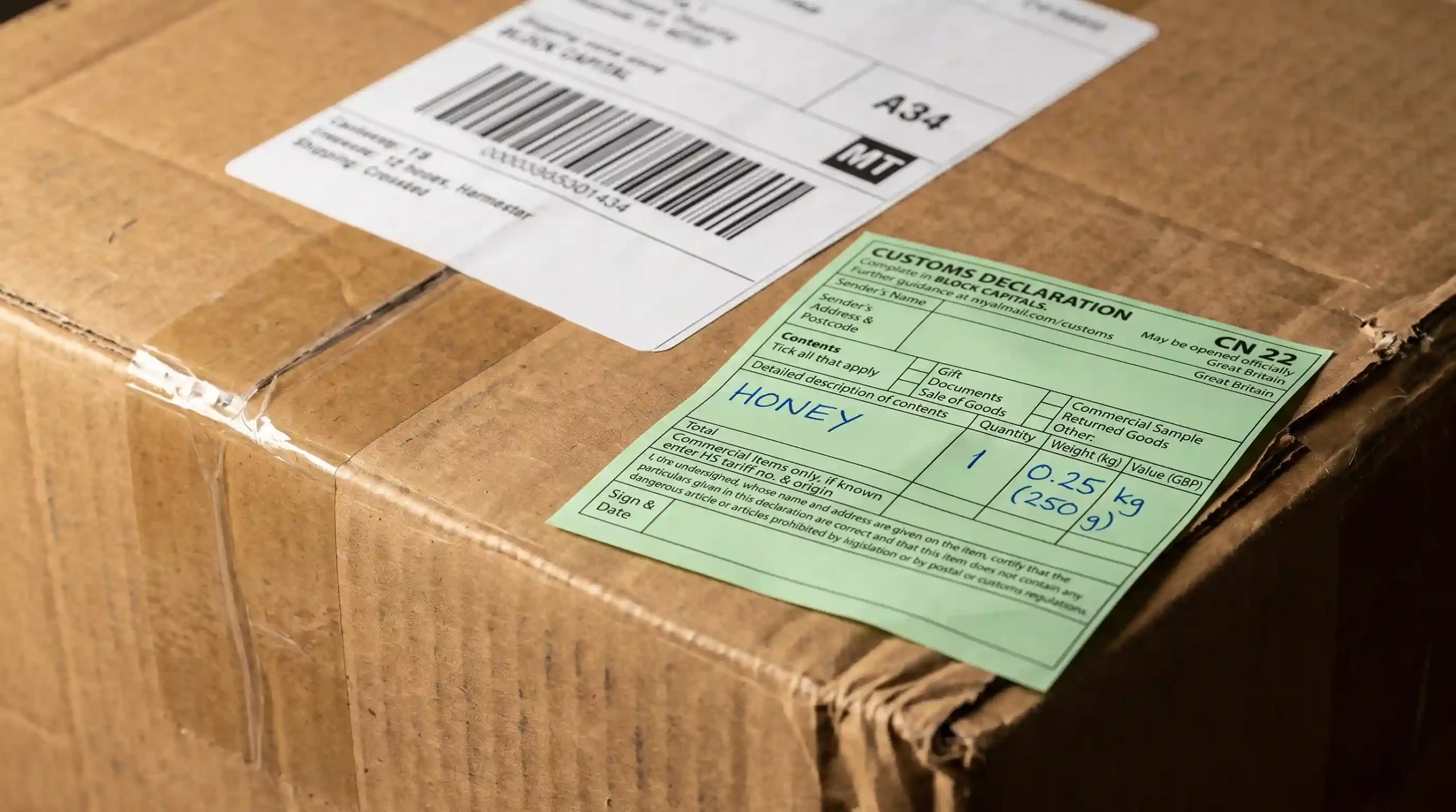 Green CN22 customs declaration form labelled honey attached to cardboard shipping box with barcode label, representing mad honey international shipping documentation